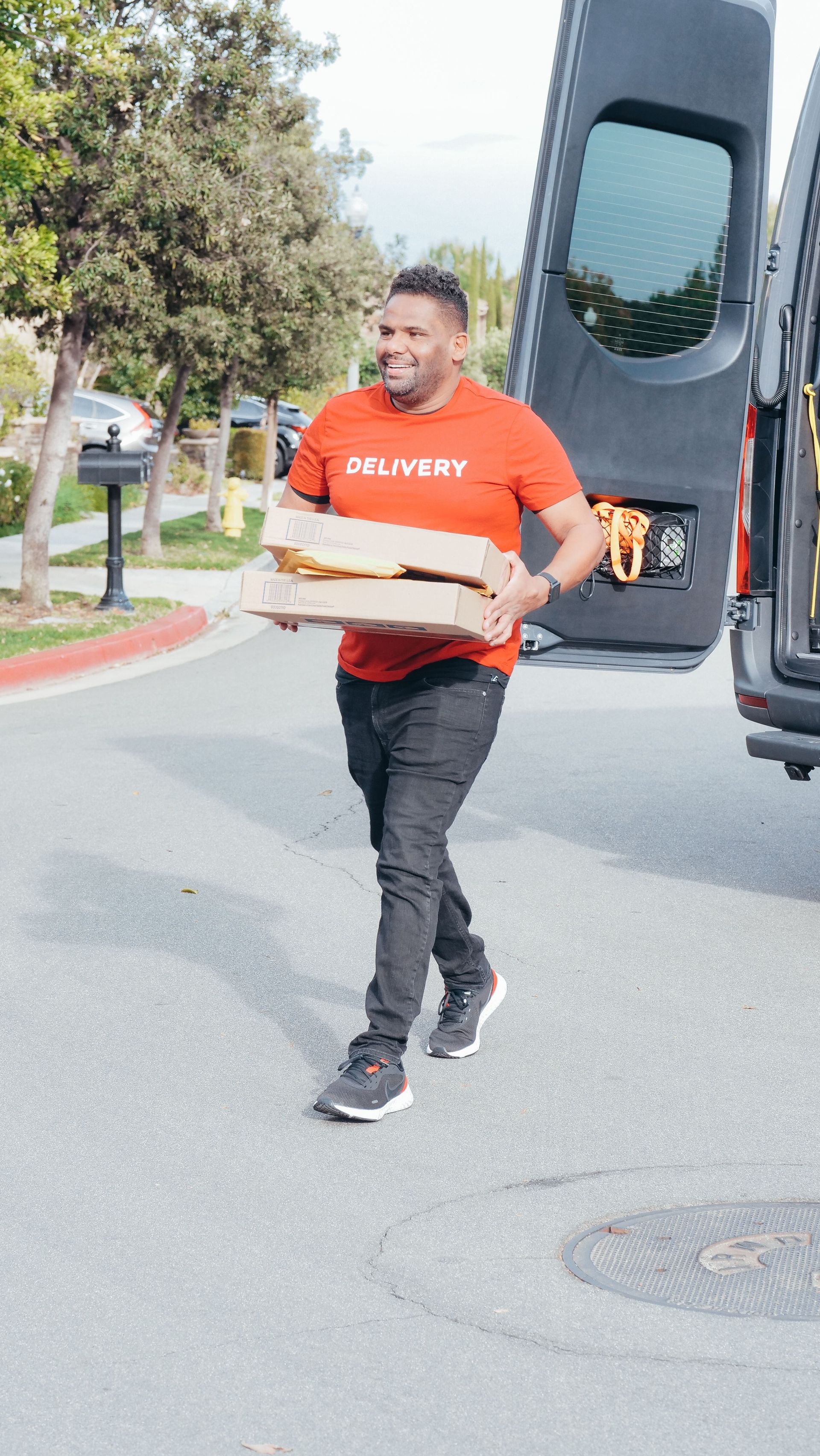 Delivery man in red shirt carrying package from van on a sunny street.