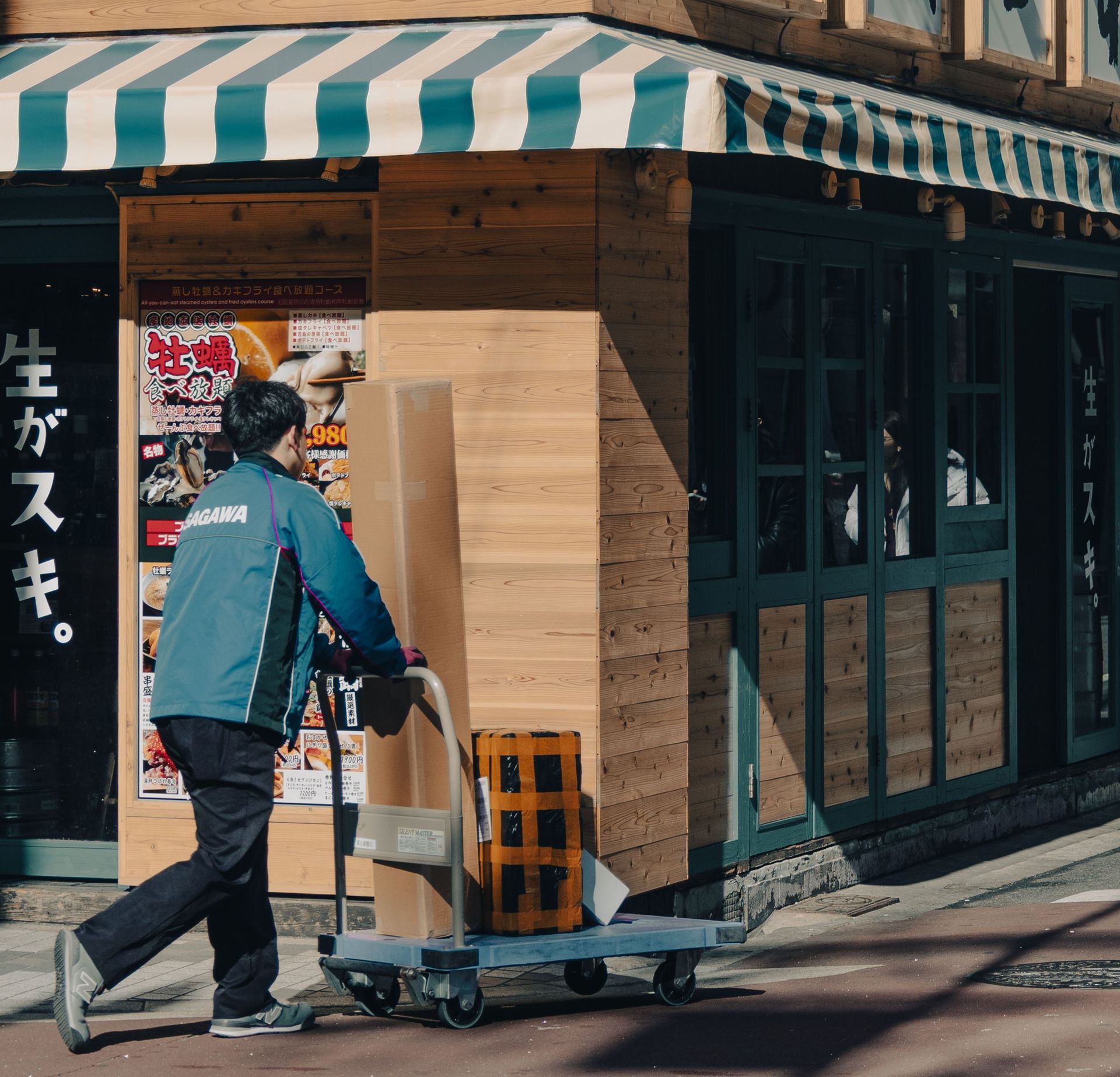 A courier pushes a cart with packages outside a wooden storefront on a sunny day.