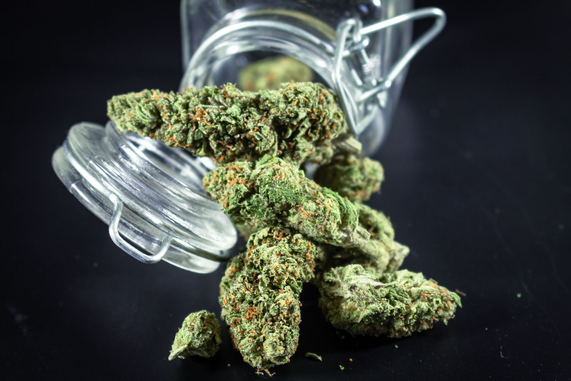 Detailed close-up of cannabis buds spilling from a glass jar, emphasizing texture and color.