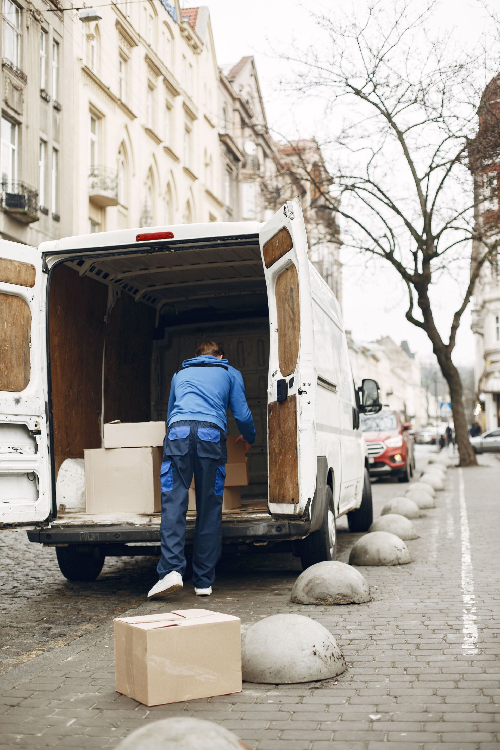 A delivery worker loads boxes into a van on a bustling city street, illustrating urban logistics.
